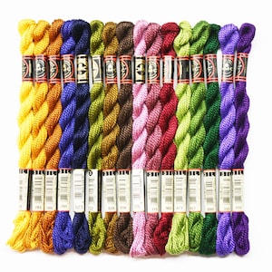 May include: A collection of 14 DMC embroidery floss spools in various colors, including gold, purple, green, brown, and pink. Each spool has a white label with black text indicating the DMC color number.