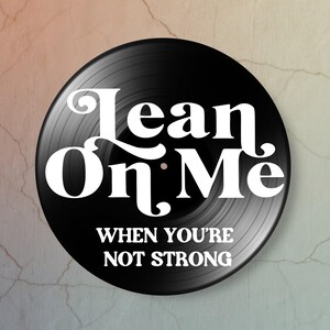 A black vinyl record with white text that reads 'Lean On Me When You're Not Strong'. The record has grooves.