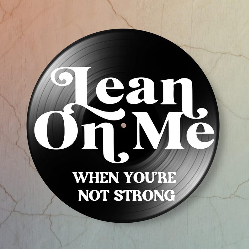 A black vinyl record with white text that reads 'Lean On Me When You're Not Strong'. The record has grooves.