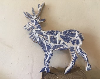 May include: A blue and white ceramic reindeer sculpture made from mosaic tiles. The reindeer is standing on a wooden base.