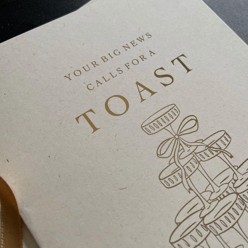 personalised your big news calls for a toast congratulations on your engagement, on ivory card with gold foil text with ivory envelope for engaged couple with tower of wine glasses.
