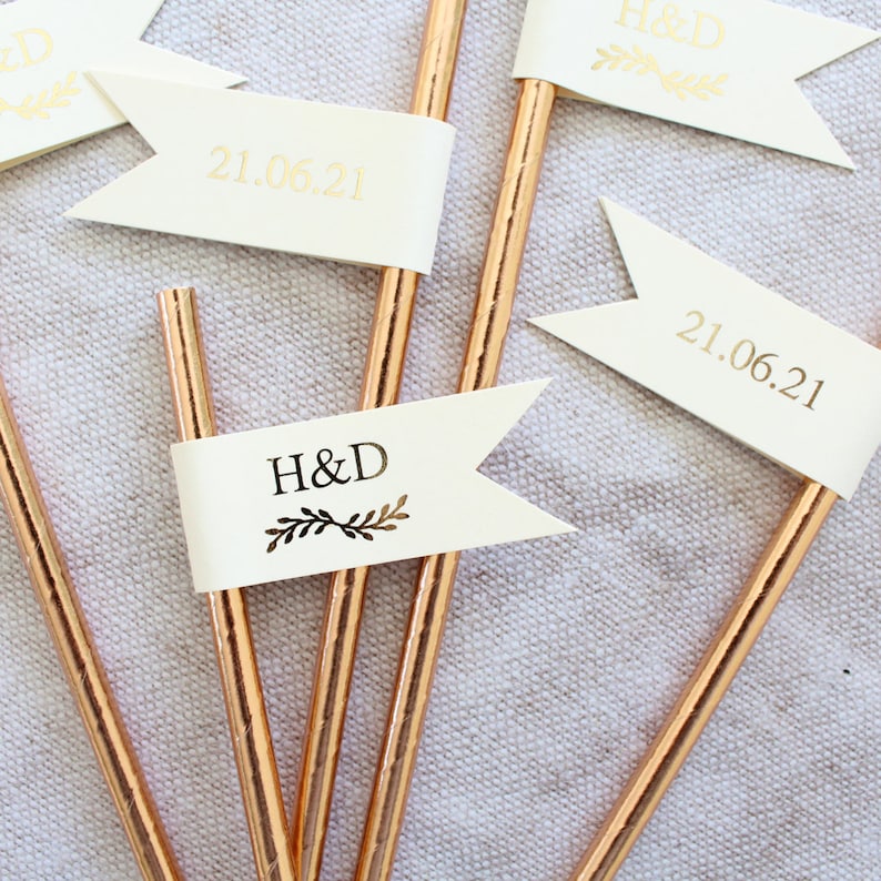 May include: Set of five gold straws with white flags. The flags have gold lettering that reads "H&D" and "21.06.21".