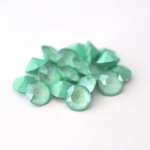 May include: A pile of light green, faceted glass rhinestones. The rhinestones are round and have a frosted finish.