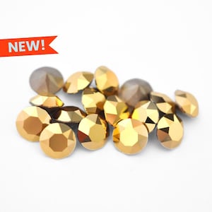 May include: A collection of faceted, golden-colored rhinestones of various shapes and sizes, scattered on a white background. Some rhinestones have a darker, more muted gold hue. A red banner with the word "NEW!" is in the upper left corner.