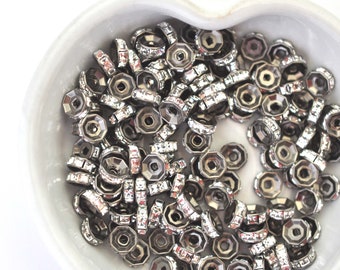 May include: A bowl filled with silver-toned metal beads. Each bead has a round, flat base and a raised, octagonal top. The beads are covered in clear rhinestones.