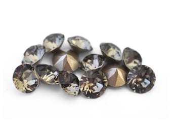 May include: A collection of faceted, smoky topaz-colored rhinestones. The gemstones vary in shape, including round and teardrop, and are scattered against a white background. The rhinestones have a reflective, sparkling quality.