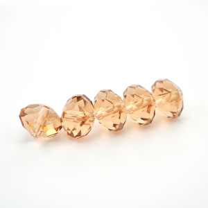 May include: Six faceted glass beads in a light amber color. The beads are round and have a smooth, polished finish.