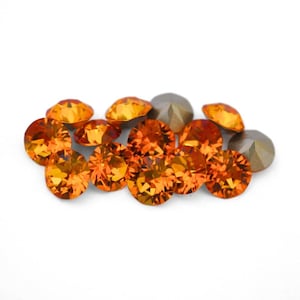 May include: A collection of orange and gray faceted gemstones. The orange stones have a brilliant cut, reflecting light. The gray stones have a more subdued, metallic appearance. The gems are scattered on a white surface.