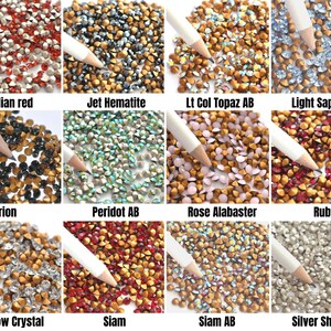 May include: Assortment of 12 colors of rhinestones, each color is displayed in a separate square. The rhinestones are small and have a pointed top. The colors are: Indian red, Jet Hematite, Lt Col Topaz AB, Light Sapphire, Morion, Peridot AB, Rose Alabaster, Ruby, Shadow Crystal, Siam, Siam AB, and Silver Shade.