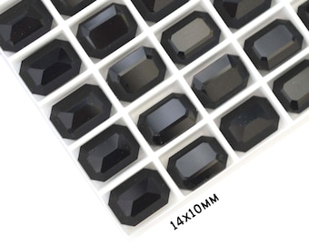 May include: A close-up of a tray of black rectangular rhinestones, each measuring 14mm by 10mm. The rhinestones are arranged in rows and columns, and the tray is white.