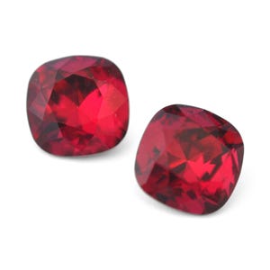May include: Two red cushion-cut gemstones with a faceted finish.