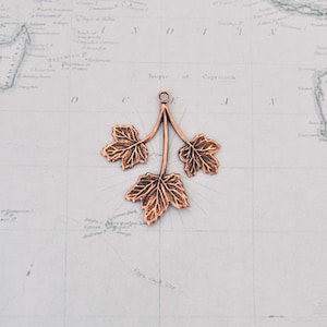 May include: A copper-colored pendant featuring a three-leaf branch with detailed leaf veins. The pendant is perfect for adding a touch of nature to jewelry projects.