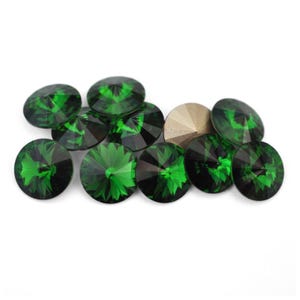 May include: A collection of emerald green, faceted, round gemstones with a gold-colored gemstone. The gemstones have a brilliant cut, reflecting light. The gemstones are arranged on a white background.