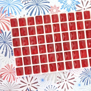 May include: A white tray with 49 red square-shaped glass tiles. The tiles are arranged in a grid pattern.