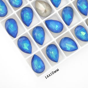 May include: A close-up view of a white tray filled with iridescent blue teardrop-shaped rhinestones. The tray is labelled "14x10mm".