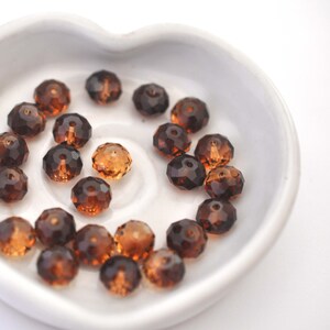 May include: A close-up of a white heart-shaped dish filled with brown glass beads. The beads are faceted and have a shiny finish.