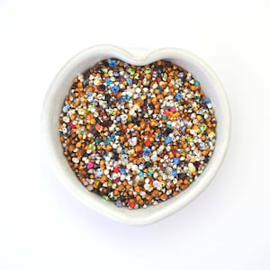 May include: A heart-shaped bowl filled with a variety of colorful rhinestones, including gold, silver, blue, red, and green.