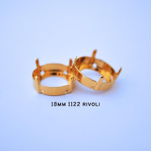 May include: Two gold-colored rivoli settings, each with four prongs and a circular base. The text "18MM 1122 RIVOLI" is printed below the settings. These settings are designed to hold 18mm gemstones.