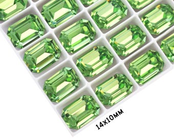 May include: A close-up of a tray of 14x10mm emerald green rectangular rhinestones. The rhinestones are arranged in rows and columns in a white tray.