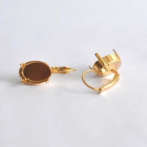 May include: A pair of gold-tone earring settings with oval-shaped bezels. The bezels are empty and ready to be filled with stones or other embellishments.