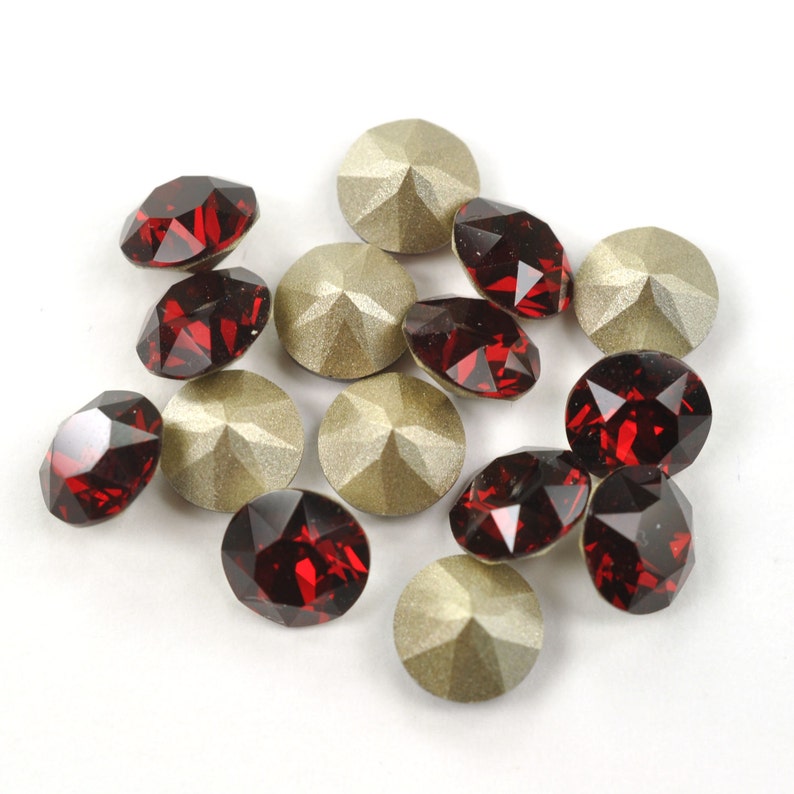 May include: A collection of red and gold rhinestones. The rhinestones are round and have a faceted design. They are arranged in a random pattern on a white background.