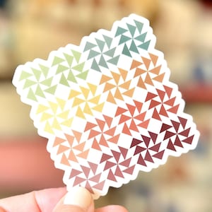 May include: A square sticker featuring a repeating geometric pattern of small triangles arranged into pinwheel shapes. The design displays a color gradient transitioning from light green and yellow at the top left to deep red and maroon at the bottom right.