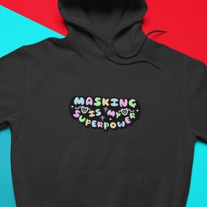Könnte beinhalten: Schwarzer Kapuzenpullover mit einer bunten Grafik, auf der "Masking is my superpower" steht.