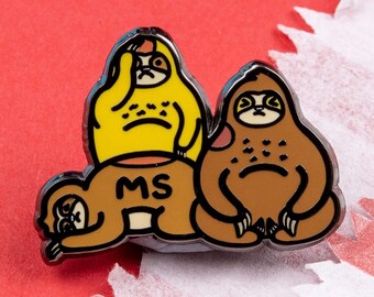 May include: Three enamel pins featuring a yellow sloth wearing a shirt that says "MS", a brown sloth, and a brown sloth wearing a shirt that says "MS".