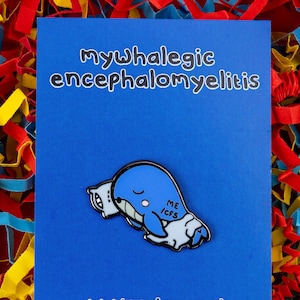 Op de afbeelding: Blauwe emaille pin van een slapende walvis met een kussen waarop "ME/CFS" staat. De pin is op een blauwe achtergrond met de tekst "mywhalagic encephalomyelitis" bovenaan en "www.innabox.co.uk" onderaan. De tekst "Volg me op sociale media!" staat onder het websiteadres, gevolgd door social media-iconen.