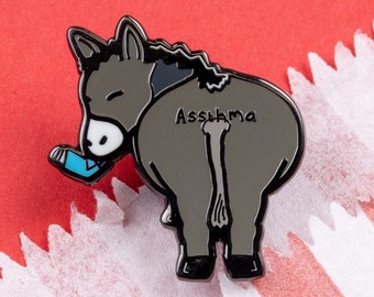 May include: Black enamel pin of a donkey with the word "Assthma" written on its back. The donkey is wearing a blue inhaler.