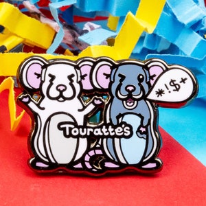 May include: A white and blue enamel pin featuring two cartoon rats. The white rat is holding its arms up in the air and the blue rat is holding a speech bubble that says "!#$+". The pin says "Touratte's" in the middle.