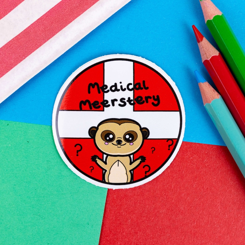 A circular sticker with white and red first aid cross as the background with a cute meerkat at the bottom with big eyes and pink cheeks and has its arms open wide. Across the top in black text reads medical meerstery.