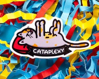 Può includere: Un adesivo bianco con un'illustrazione di un gatto di cartone con gli occhi chiusi e le zampe in aria. Il gatto è sdraiato sulla schiena su un oggetto rosso. L'adesivo ha il testo "CATAPLEXY" su uno stendardo nero.