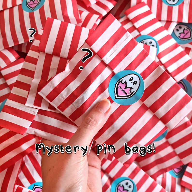 Mystery Enamel Pin Bags in a pile. Red & white stripe candy bags with a innabox ghost logo sticker with text reading mystery. Surprise goodie bag of three enamel pins raising awareness for hidden disabilities and invisible illnesses.