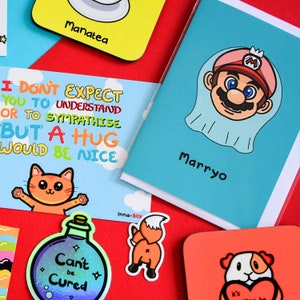 Marryo - Mario Engagement Wedding Card on red background with other innabox products. Blue a6 congratulations card of a smiling nintendo mario character head wearing a white bridal wedding veil, underneath him is black text reading Marryo.