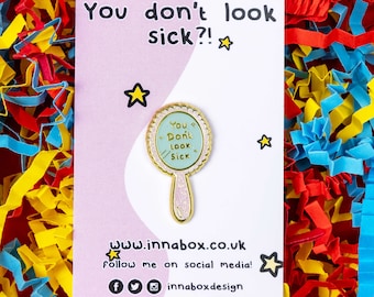 May include: A pink and white card with the text "You don't look sick?!" and a gold mirror pin with the text "You Don't Look Sick" on a blue background.