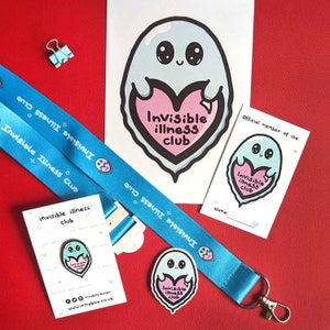 May include: A blue lanyard with the text "Invisible Illness Club" printed on it. The lanyard has a small blue ghost charm with a pink heart that says "Invisible Illness Club". There is also a small card with the same ghost design and text. The card says "Official member of the: Invisible Illness Club".