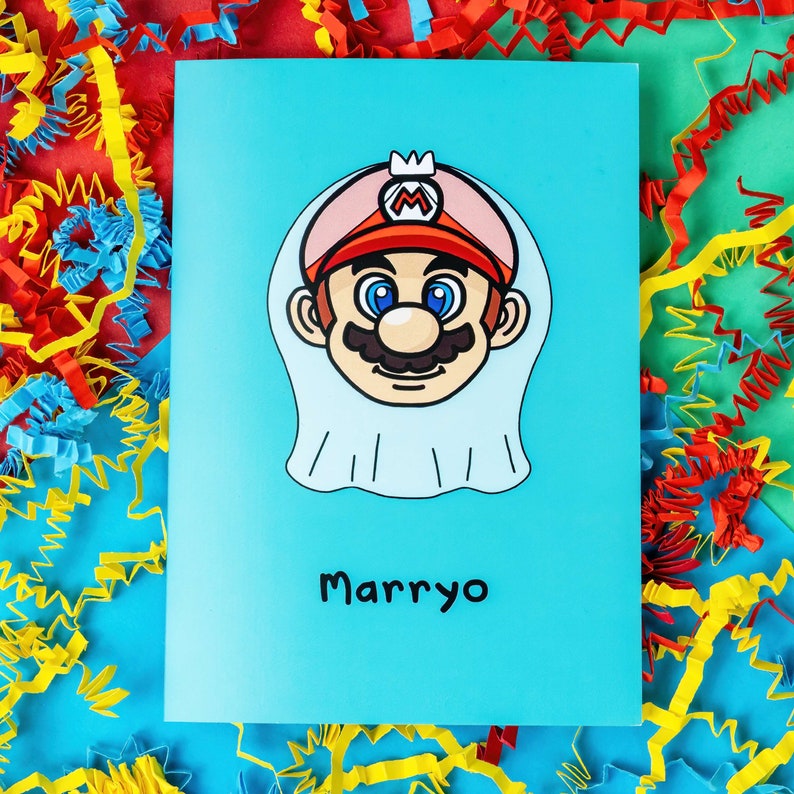 Marryo - Mario Engagement Wedding Card on red, blue & green card with crinkle card confetti. Blue a6 congratulations card of a smiling nintendo mario character head wearing a white bridal wedding veil, underneath him is black text reading Marryo.