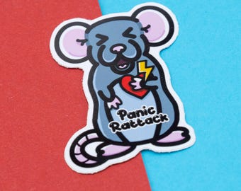 Könnte beinhalten: Eine graue Comic-Ratte mit rosa Nase und Ohren hält ein rotes Herz mit einem gelben Blitz hindurch. Die Ratte schaut mit einem überraschten Ausdruck nach oben. Der Text "Panic Rattack" steht unter der Ratte.
