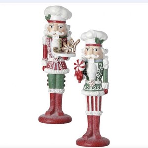 Puede incluir: Dos figuritas de cascanueces festivas vestidas de chefs. Una sostiene un plato con una galleta de jengibre que dice "Joy" y un copo de nieve. La otra sostiene un bastón de caramelo.