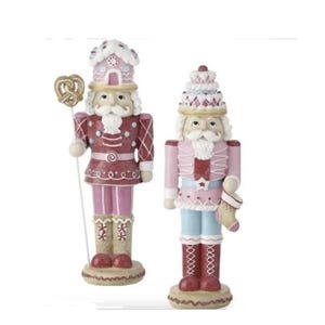 Puede incluir: Dos figuras de cascanueces de Navidad de color rosa y rojo con decoraciones de temática de dulces. El cascanueces de la izquierda sostiene un pretzel y el cascanueces de la derecha sostiene una media.