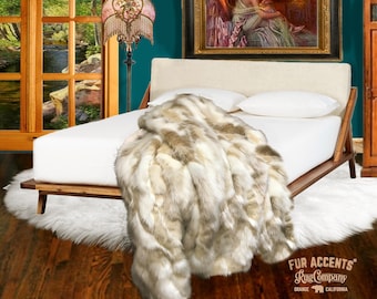 May include: A white faux fur throw blanket with brown accents is draped over a bed with white linens. The bed is made of wood and has a headboard. The room is decorated with a teal wall, a painting, and a lamp with a pink and white shade.