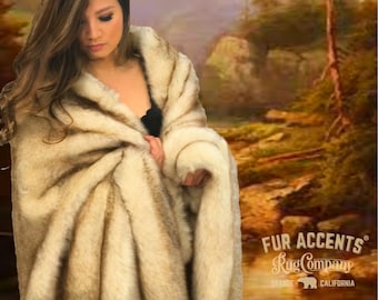 May include: A faux fur throw blanket in shades of cream and brown, draped over a person. The blanket has a soft, textured appearance. The Fur Accents Rug Company logo is visible in the bottom right corner.