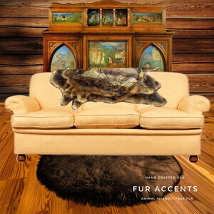 May include: A light brown faux fur throw rug on a beige sofa with a dark brown faux fur round rug on the floor. The sofa is in front of a wooden cabinet with glass doors and paintings inside. The text "HAND CRAFTED USA FUR ACCENTS ANIMAL FRIENDLY FAUX FUR" is at the bottom of the image.