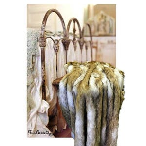 May include: A faux fur throw blanket in brown, white, and black with a long, shaggy pile. The blanket is draped over a wooden stool in front of a vintage iron bed frame.