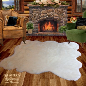 Op de afbeelding: Witte nep-bontkleed met een ruwe textuur, gelegd op een houten vloer voor een stenen open haard. Het kleed heeft een natuurlijke, onregelmatige vorm. De tekst "FUR ACCENTS Rug Company ORANGE CALIFORNIA" is zichtbaar in de linkerbenedenhoek van de afbeelding.