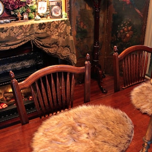 Puede incluir: Dos sillas de madera con cojines de asiento de piel sintética marrón en una habitación con chimenea y suelo de madera. Las sillas están delante de una mesa de madera con una vela encima. El texto "fur accents" es visible en la esquina inferior izquierda de la imagen.