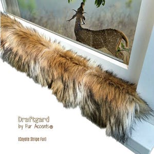 May include: A brown, black, and white faux fur draft guard with the text "Draftgard by Fur Accents® (Coyote Stripe Fur)" on a white surface.
