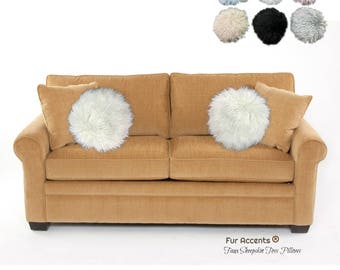 May include: A tan sofa with two white faux sheepskin toss pillows and two matching square pillows. Above the sofa are several round faux sheepskin pillows in various colors. The text "Fur Accents Faux Sheepskin Toss Pillows" is at the bottom.