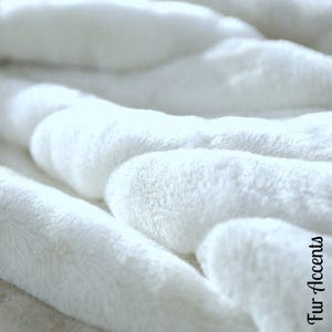 Può includere: Primo piano di una coperta in pelliccia sintetica bianca. La coperta è morbida e soffice, con una sensazione di lusso.